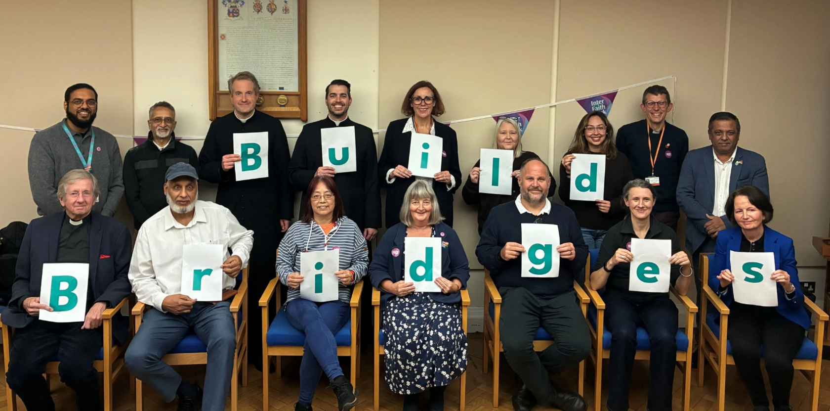 People of all different ethnicities sit on chairs and hold signs which read "Build Bridges".