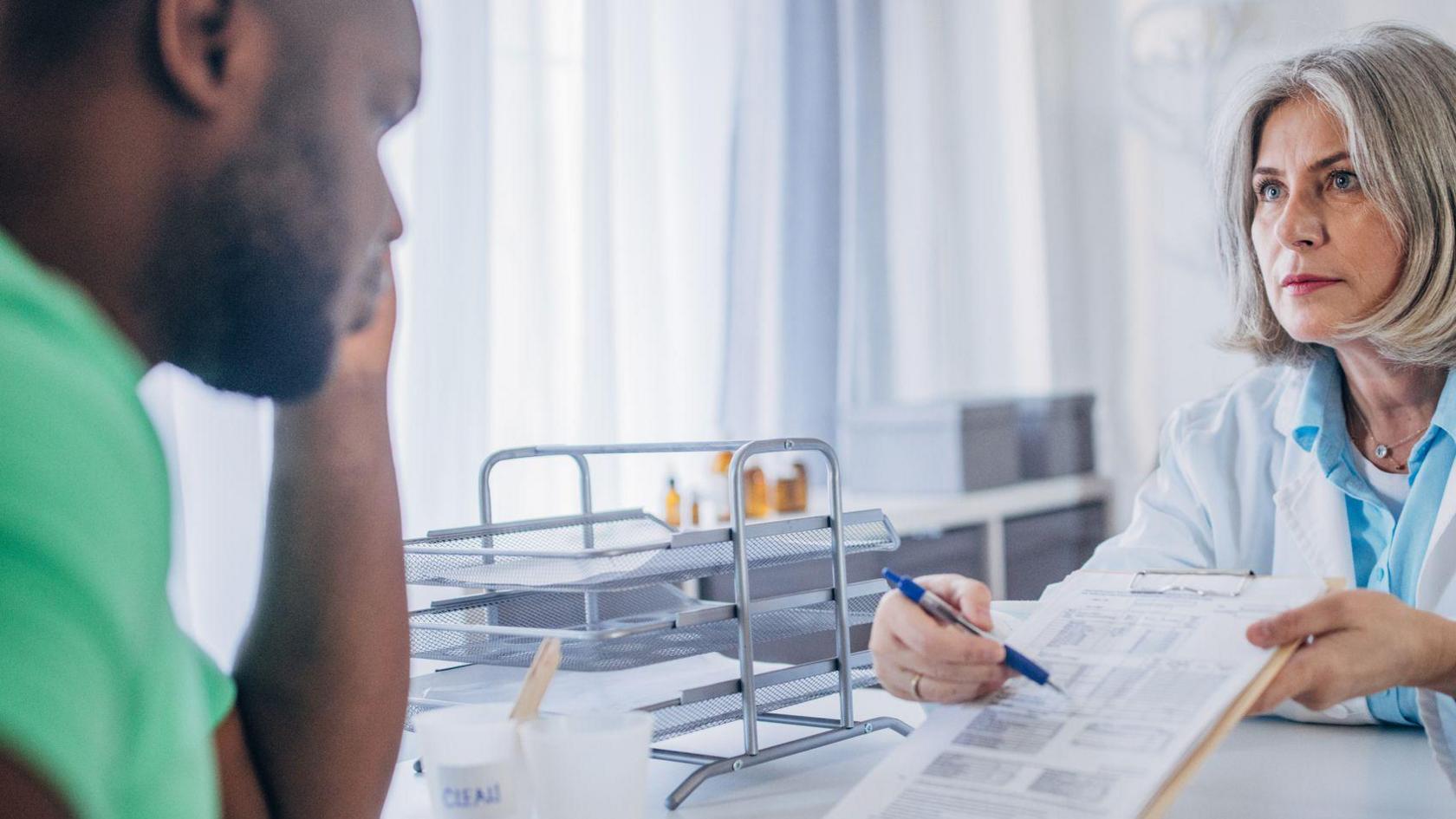 A medical professional shows a form on a clipboard to a man 