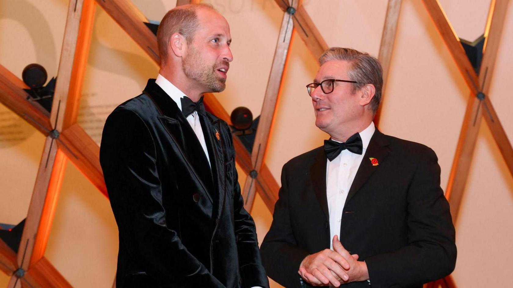 The Prince of Wales and Prime Minister Sir Keir Starmer, both wearing dark dinner jackets and bow ties, talk with each other at an event.