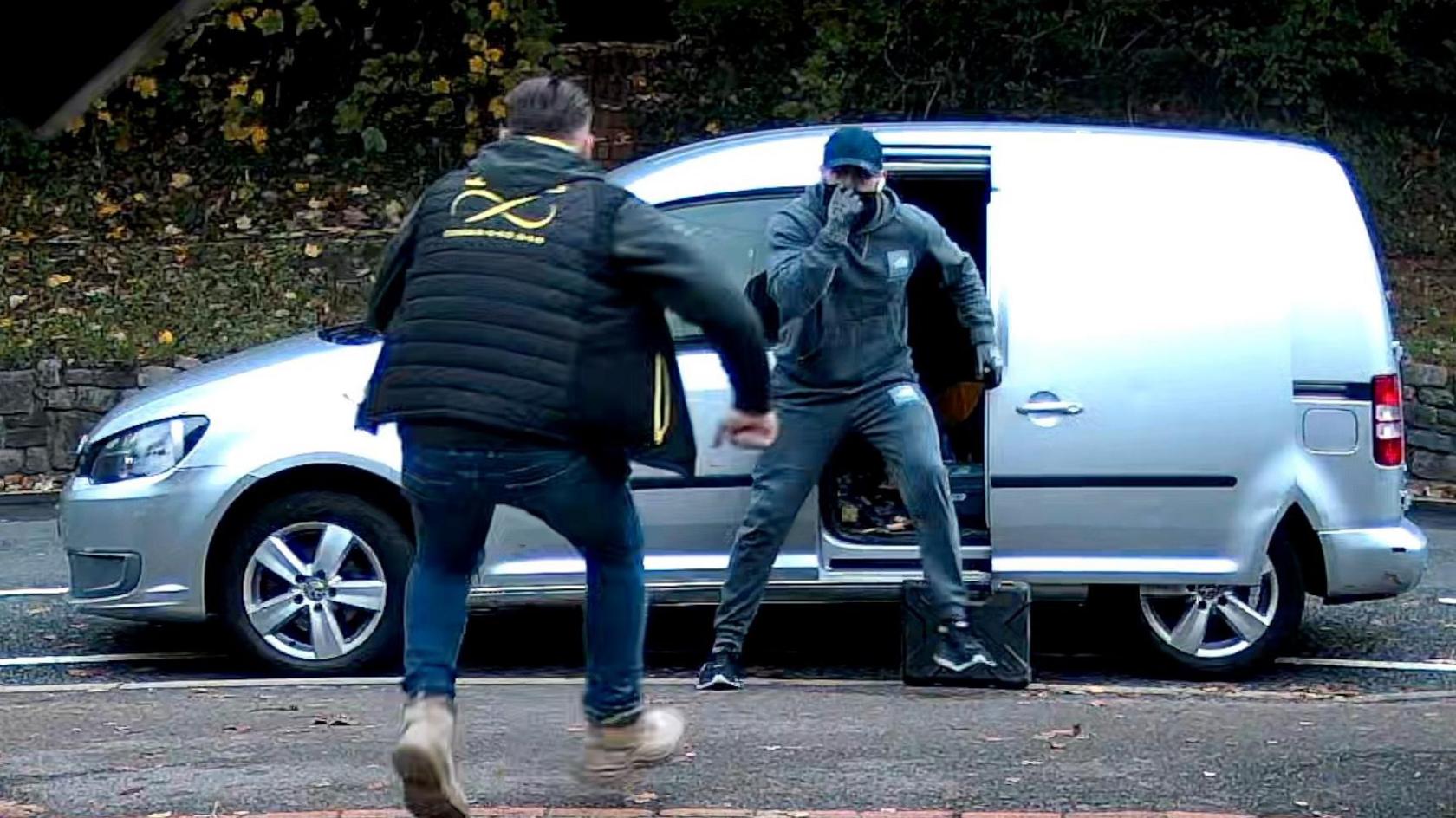 An image take from CCTV shows Steve Piller running towards a man with his face covered, who's standing in front of a silver van with a box of tools at his feet.