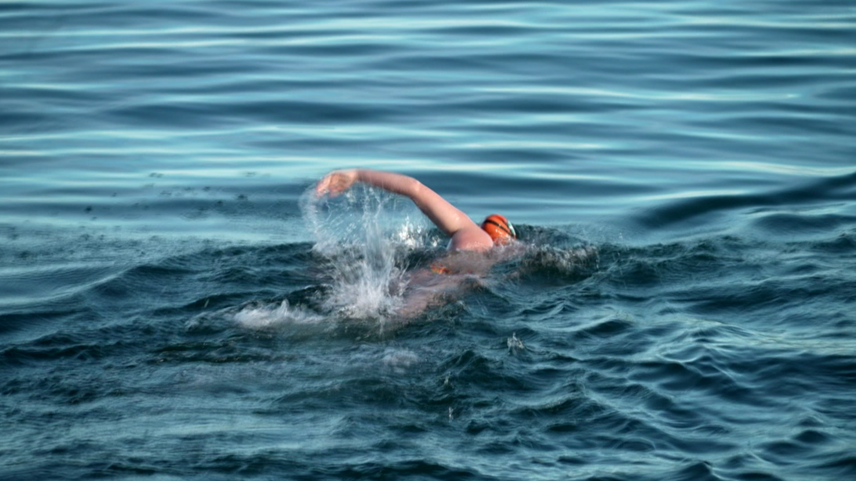 A young girl with an orange swimming cap doing front crawl in the sea.