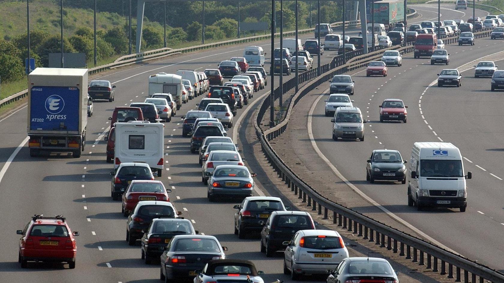 Heavy traffic on a three-lane motorway, which bends around to the right.