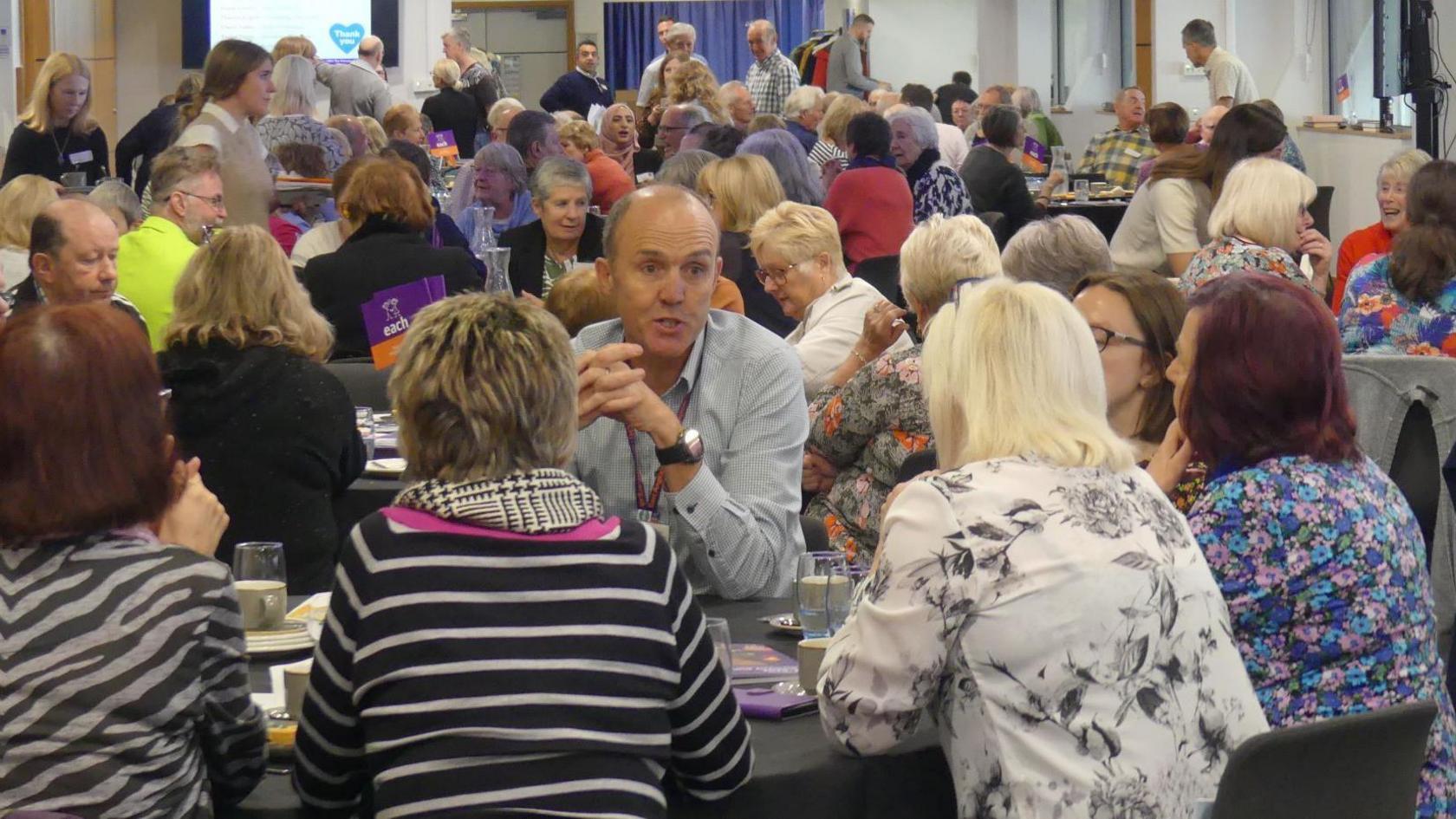 Large group of people at tables talking and laughing with each other.