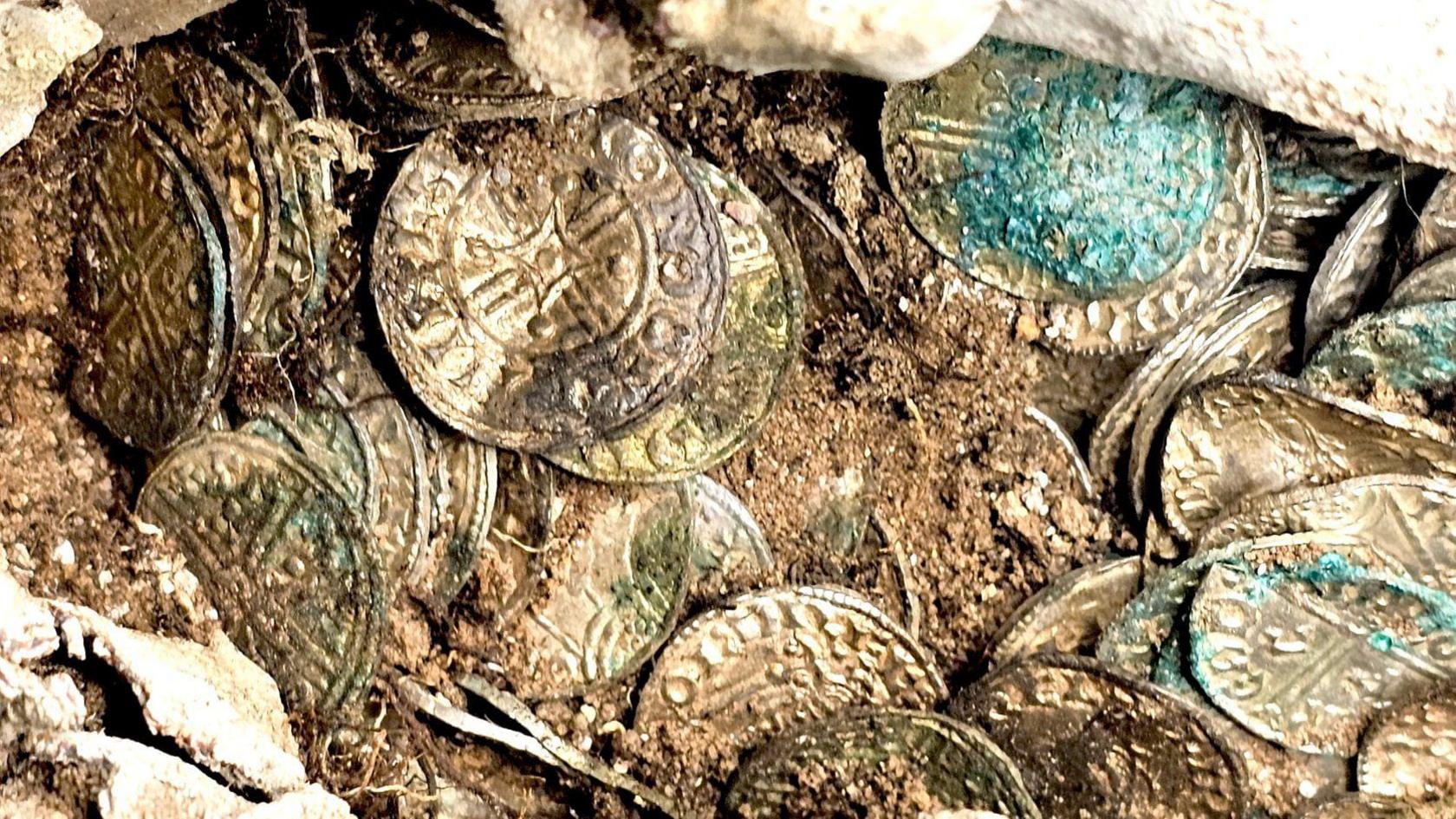 A closer view of the coins. They rest around and on top of each other and some dirt sits in the collection. 