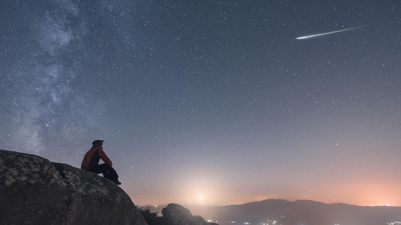 A person sitting on a hill looking at a meteor shower