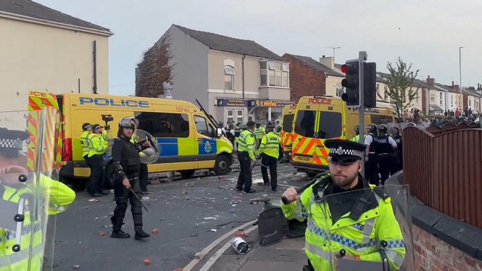 Riot police holding shields in front of three riot police vans in Southport 