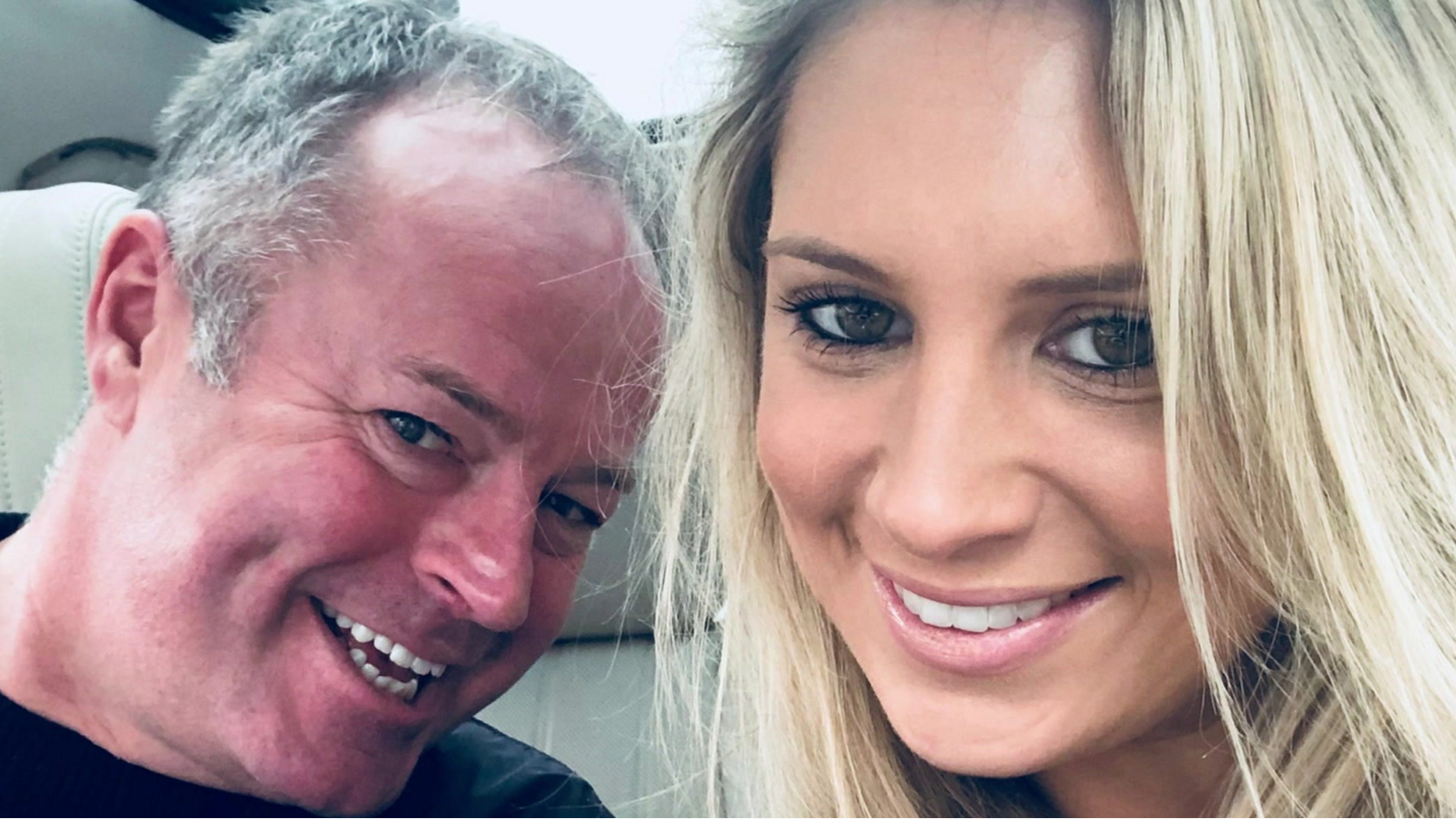 A closely-cropped selfie image of a smiling woman with long blonde hair and a smiling man with greying hair. The background of beige leather seats suggest they are possibly sitting in the front of a car.
