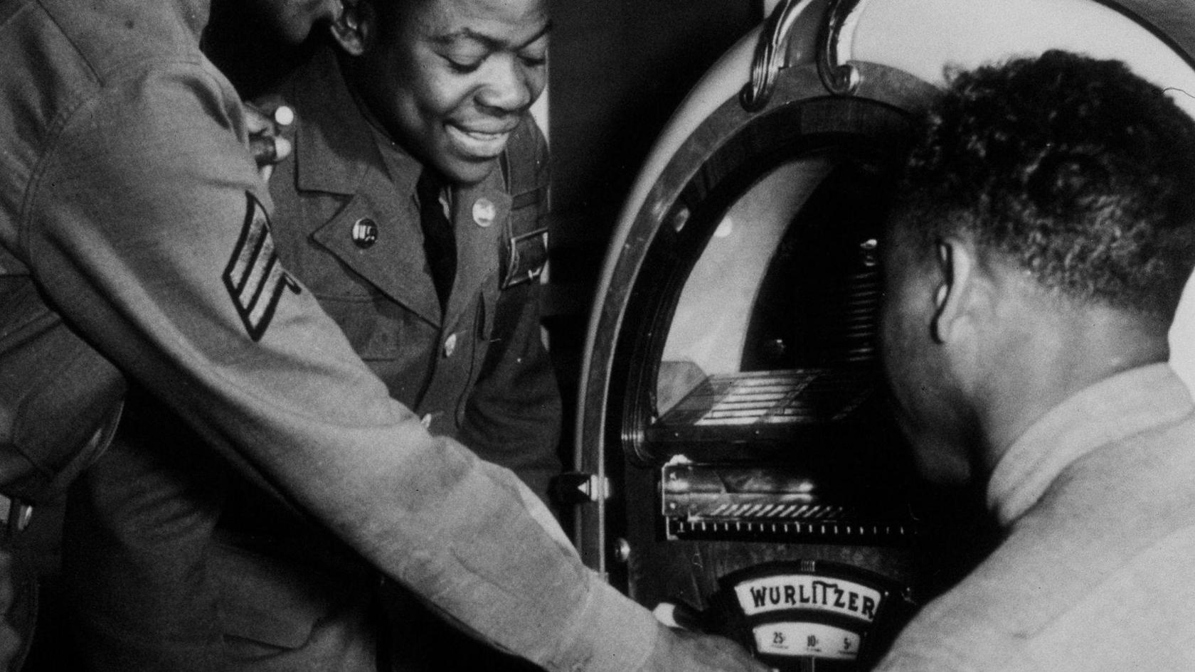 A black and white image of American servicemen selecting songs on a Wurlitzer jukebox.