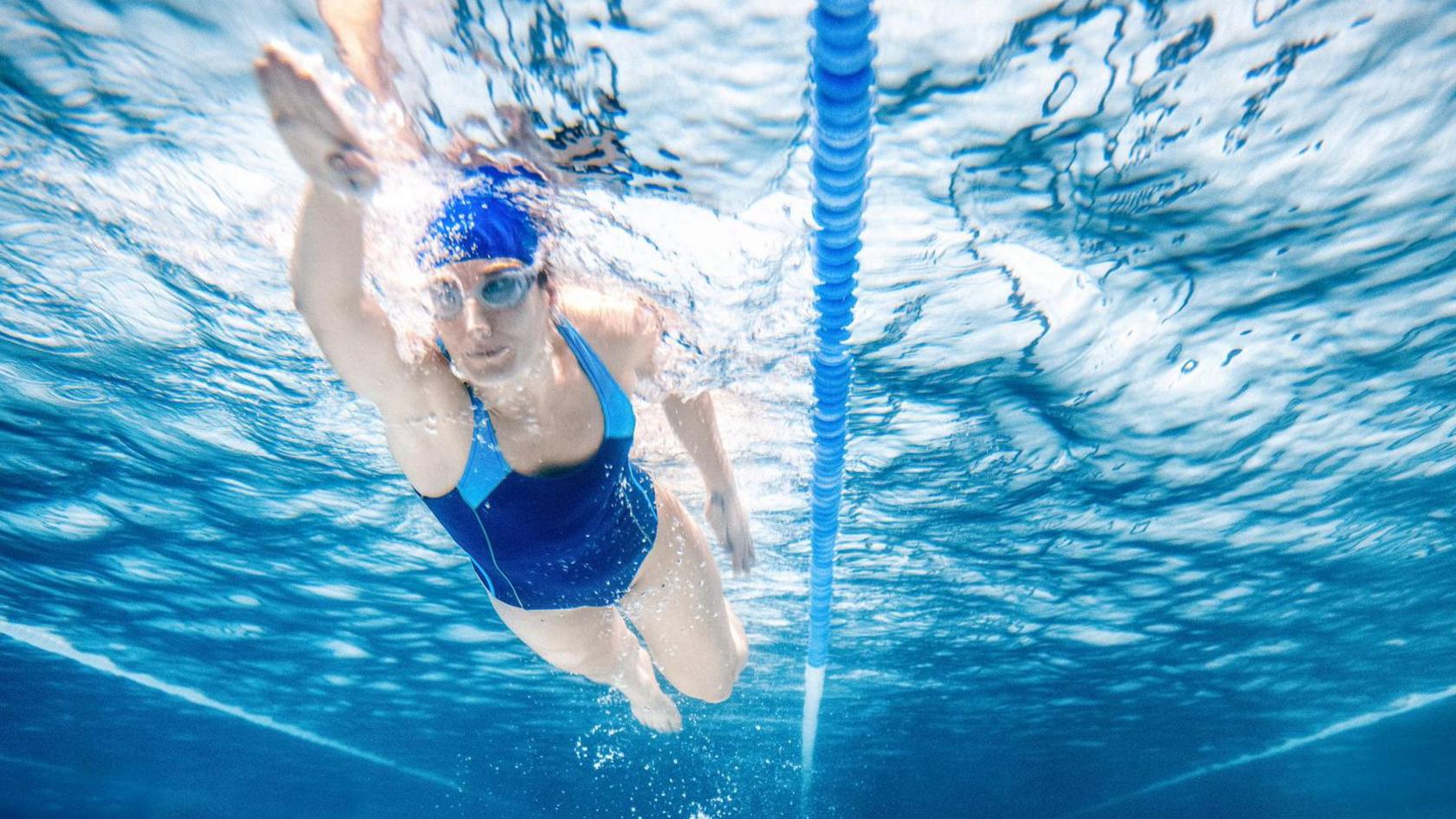 A woman is wearing a blue swimming costume and is swimming underwater