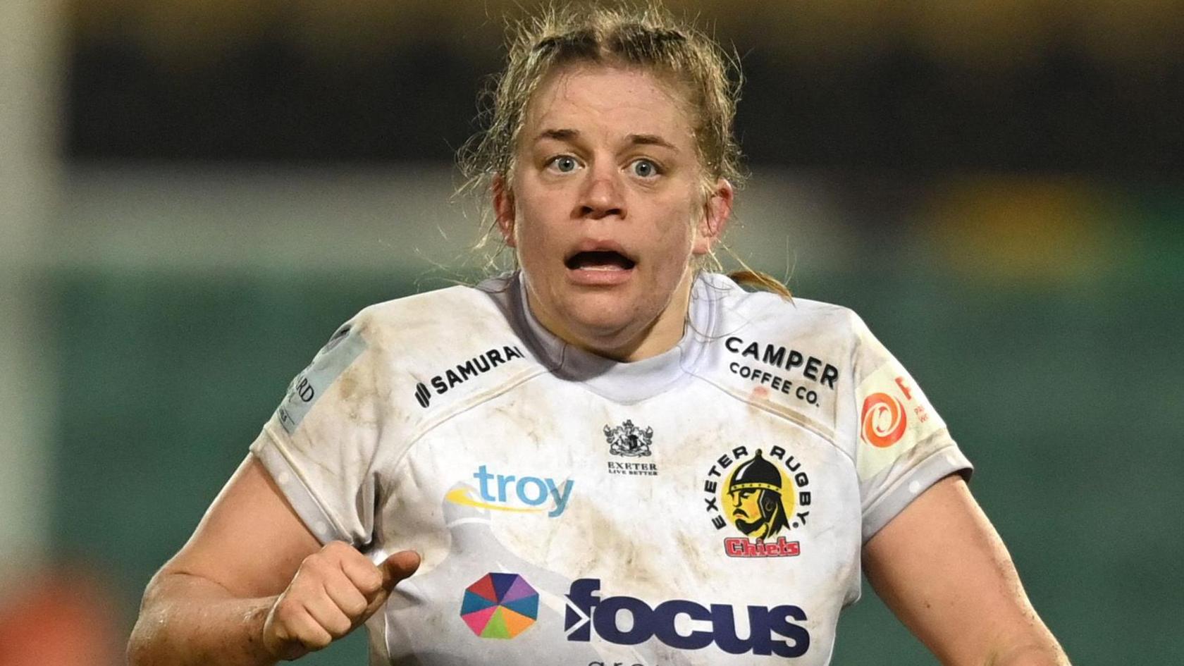 Emily Tuttosi wearing a white Exeter Rugby shirt with different logos on the front in action for the club.