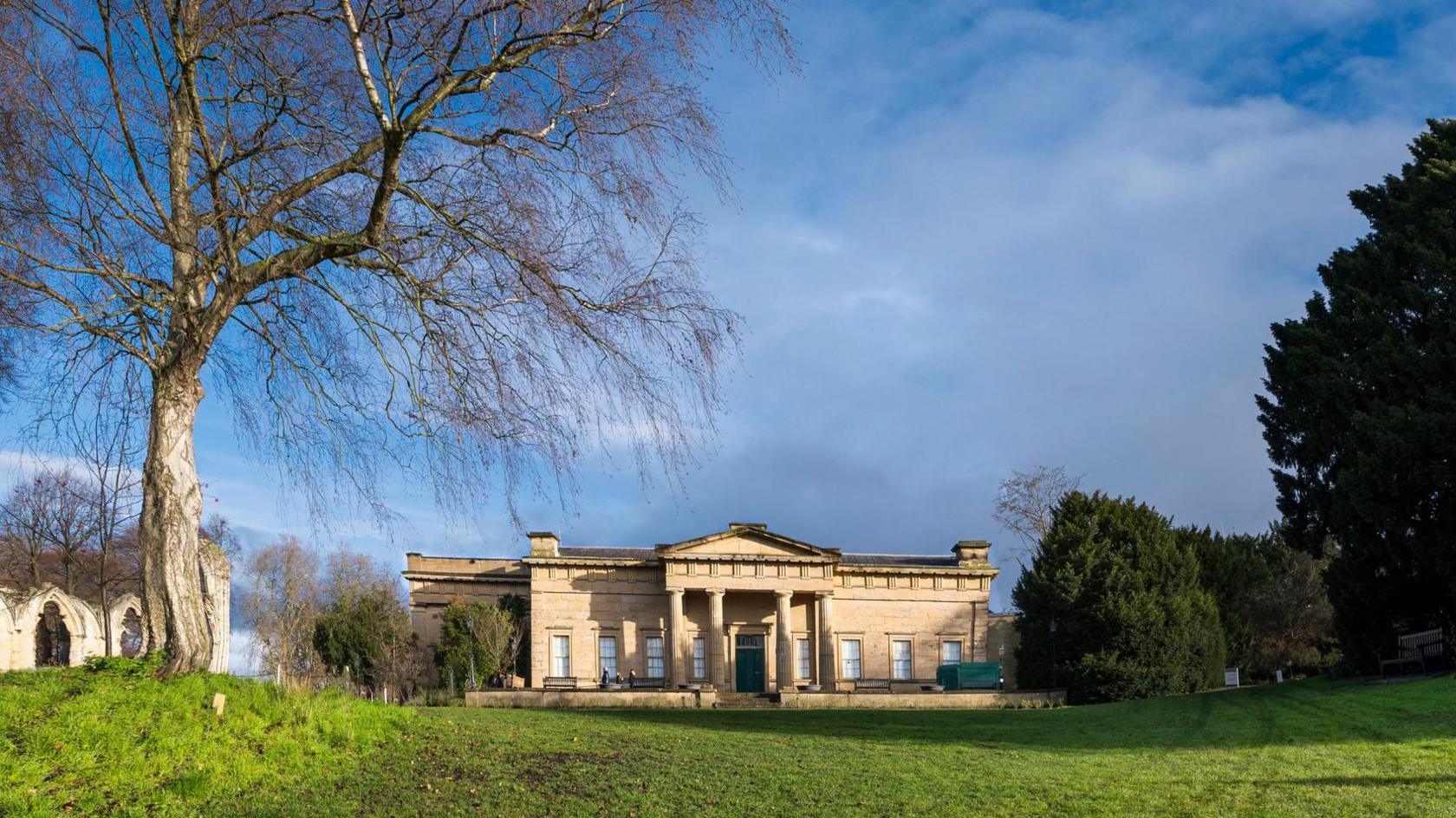 Yorkshire Museum stone building with pillars sits in green park-style space flanked by trees