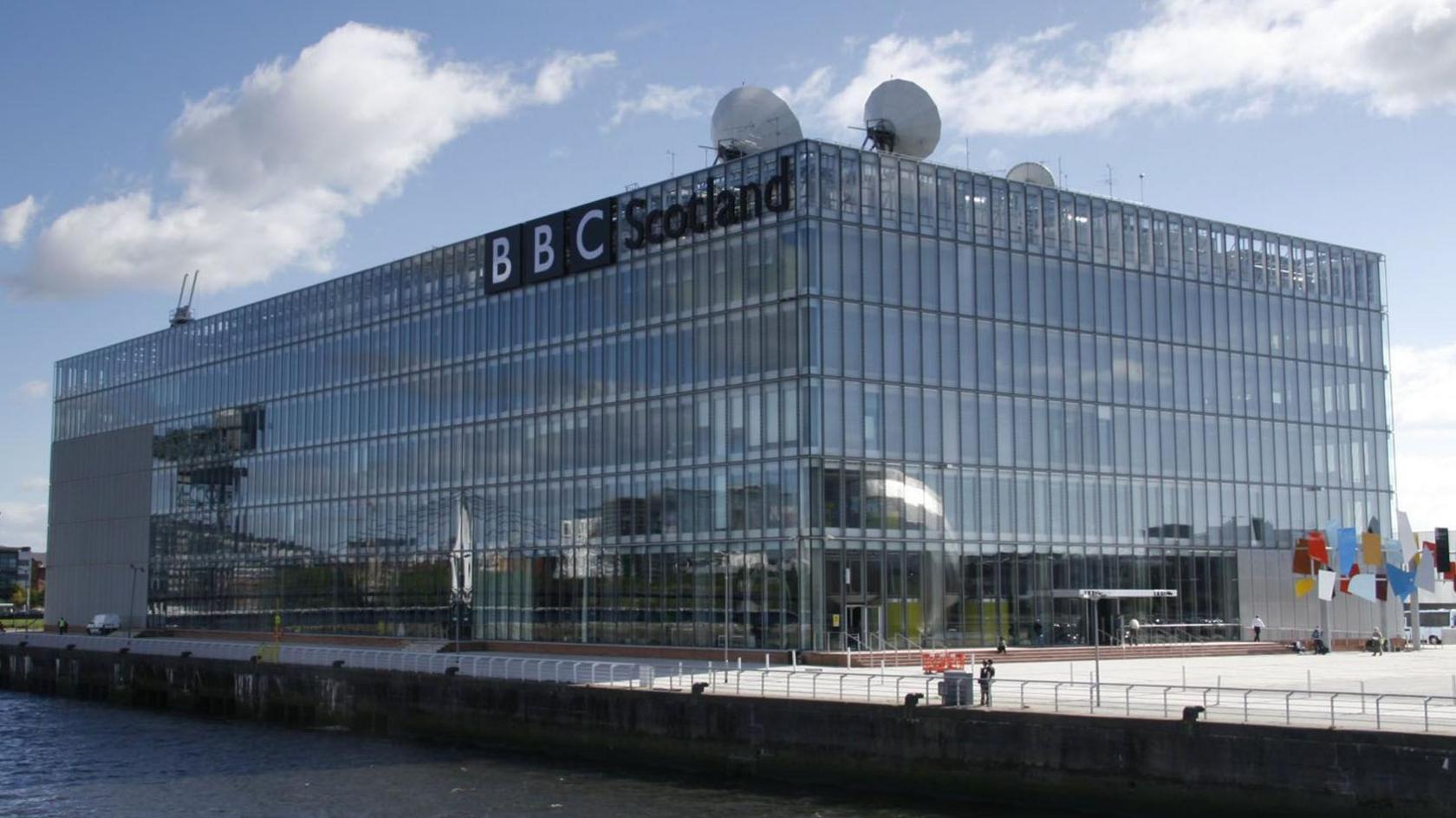 A large glass box building with a BBC sign and satellite dishes on top