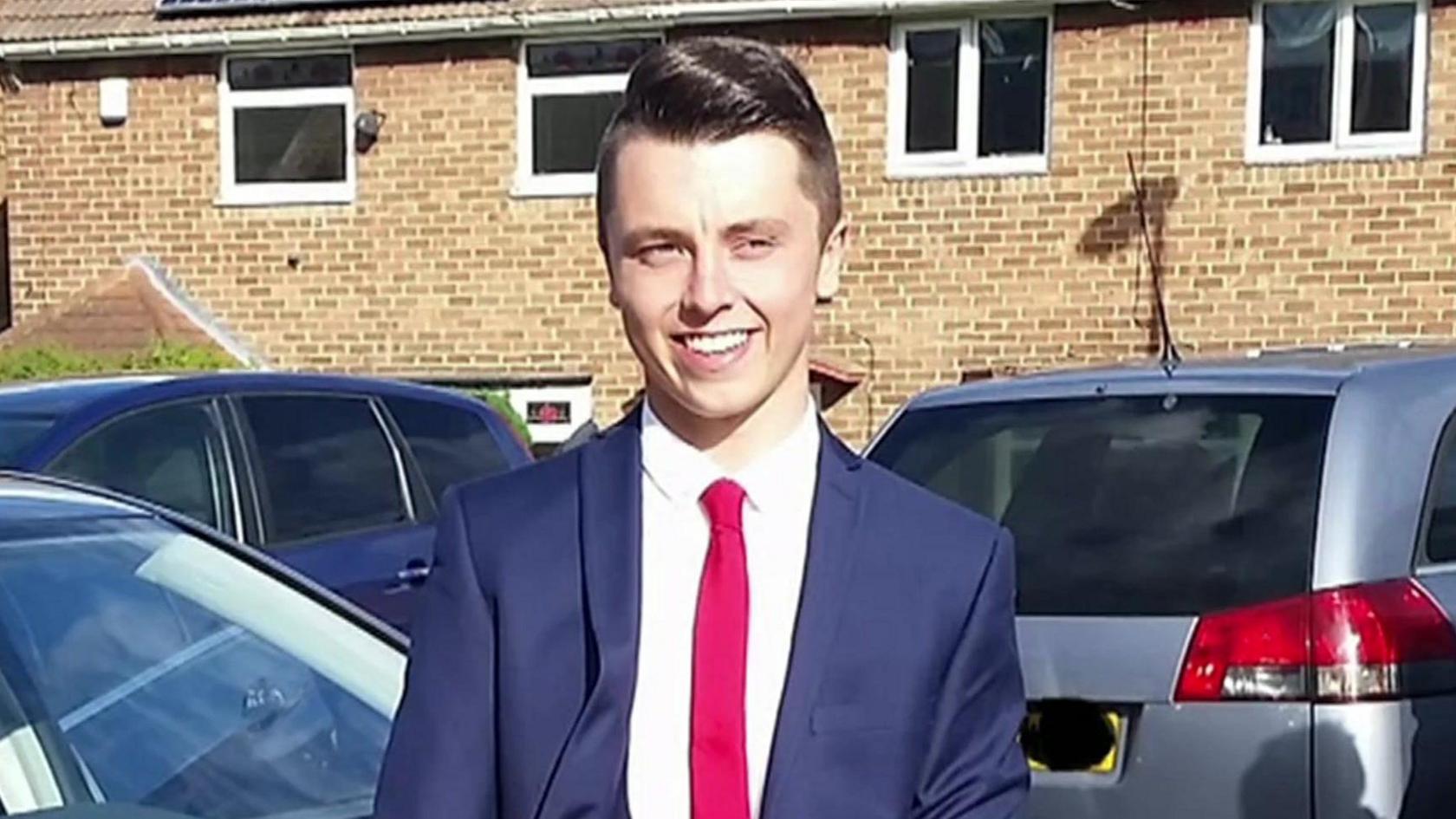 A picture of Connor Brown. He has short dark hair, is wearing a blue suit, white shirt and red tie