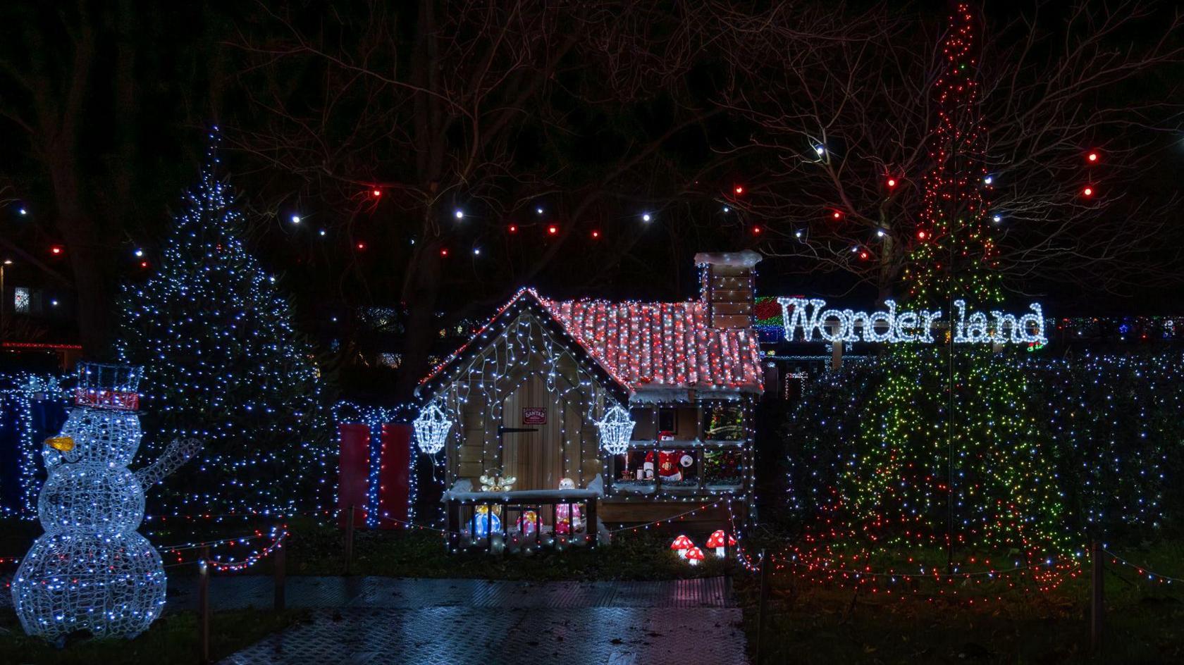 A grotto display in Sarum Avenue, Melksham, Wiltshire. Two large Christmas trees are planted either side of the grotto and there are large presents and a snowman light. The word "Wonderland" is also spelled out in lights. 