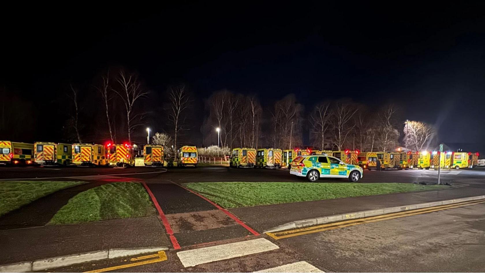 Seventeen ambulances lined up outside Gloucestershire Royal Hospital at night.