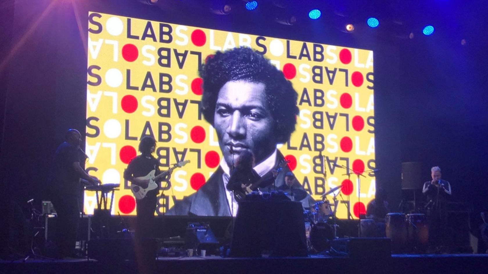 A rehearsal of the Belfast show North Star, featuring musicians and a large image of abolitionist Frederick Douglass on the screen behind he stage