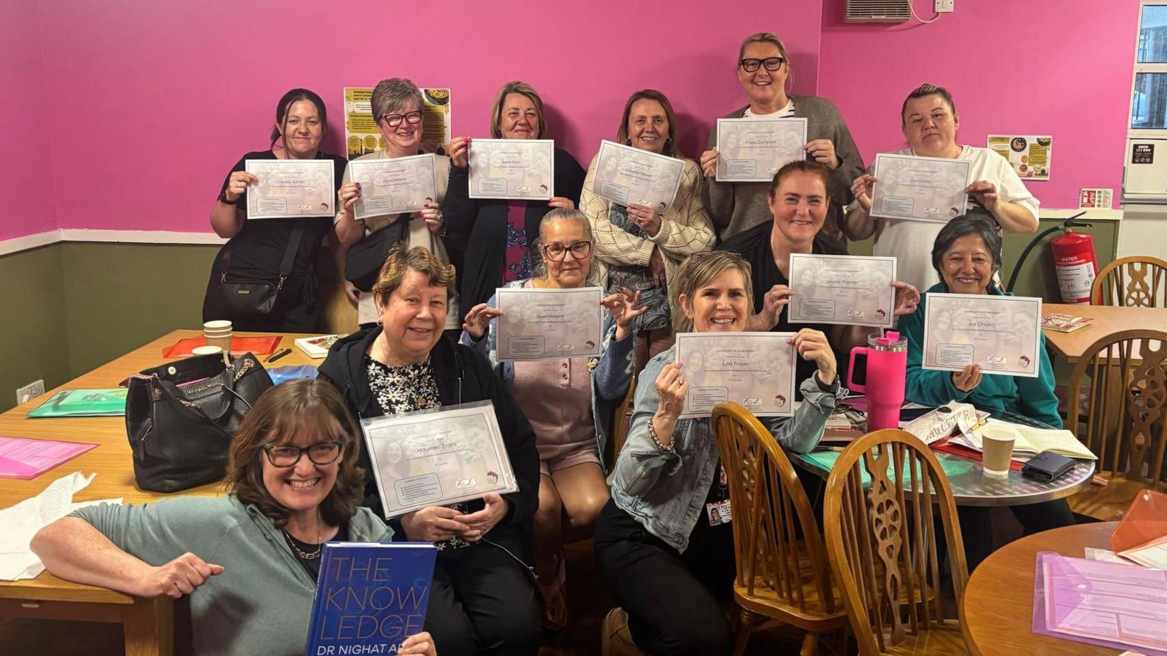 A group of 12 women at the Menopause Hub holding up certificates after completing menopause champion training. They are all smiling.