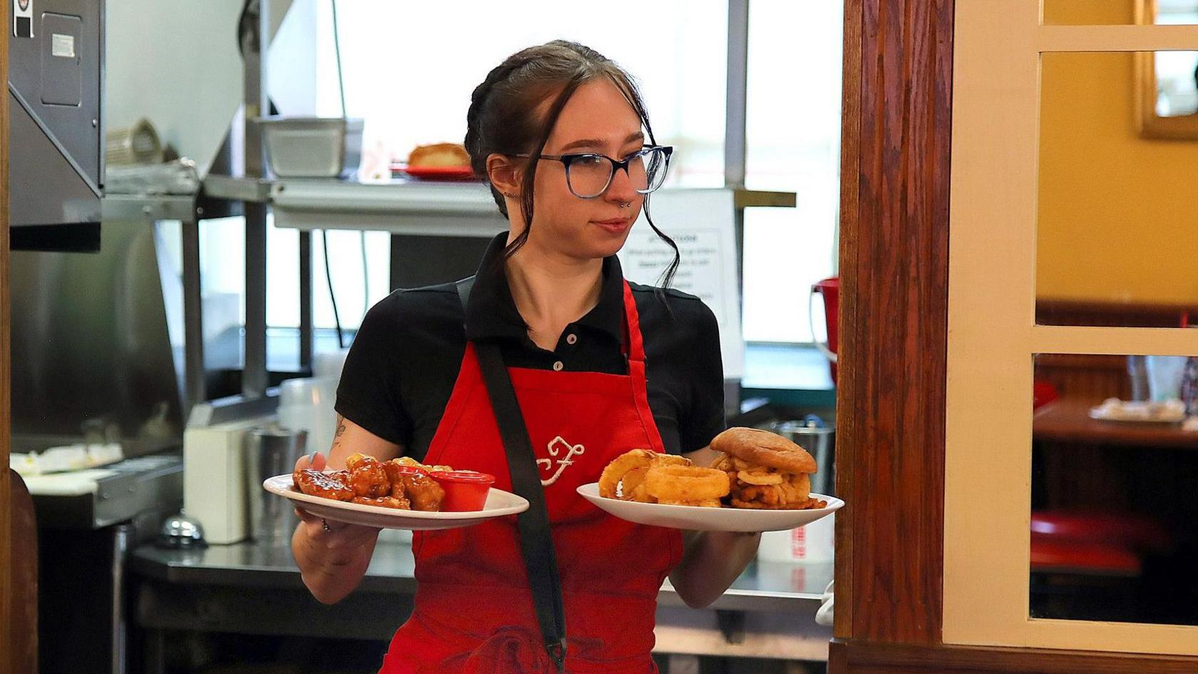 A waitress in the US wearing a red apron with the letter F on the front, bringing out two plates of food