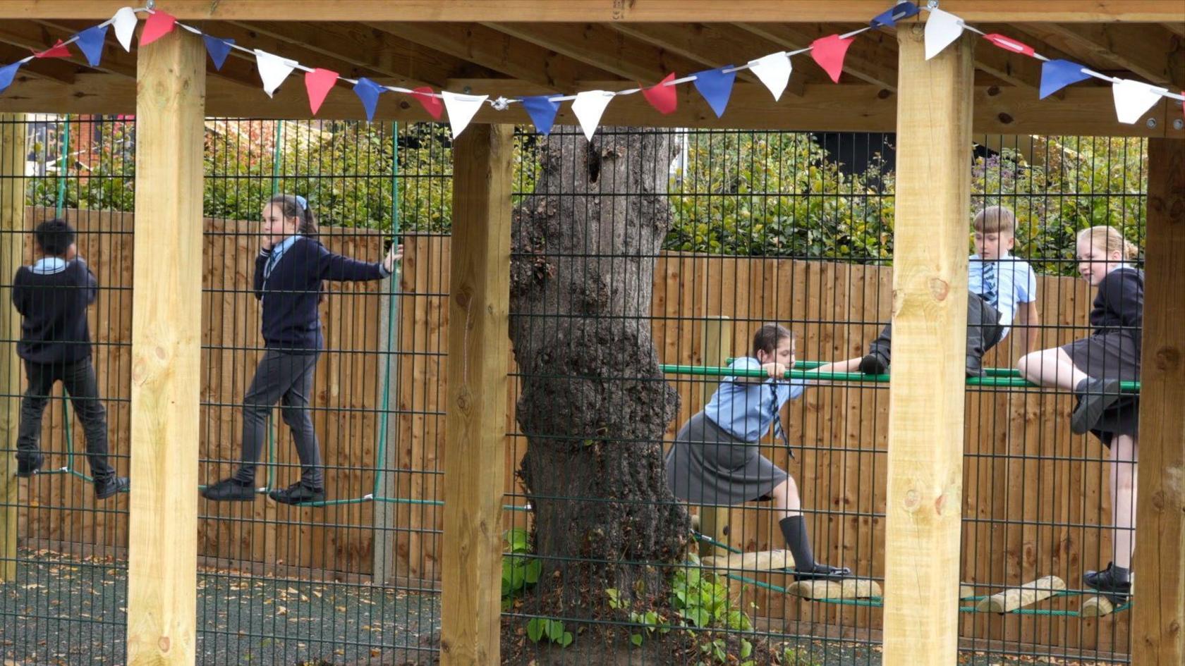 Children play on play equipment which includes agility trails connected by ropes/