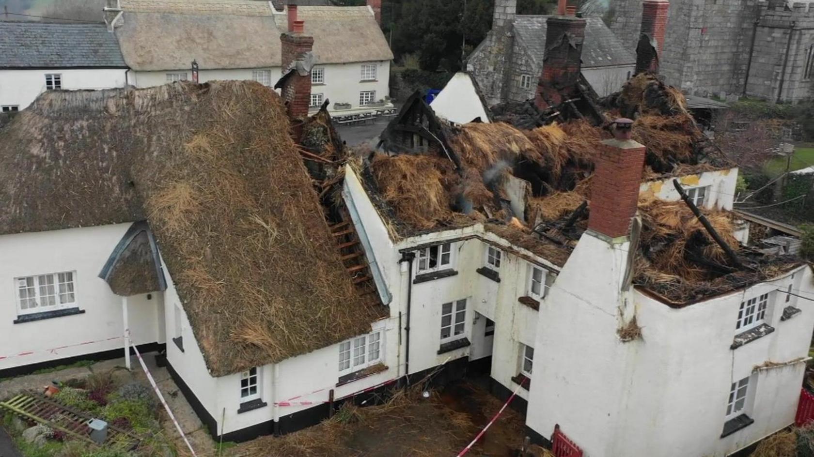 An aerial view of the three adjoining white cottages shows severe damage to the thatched roofs.