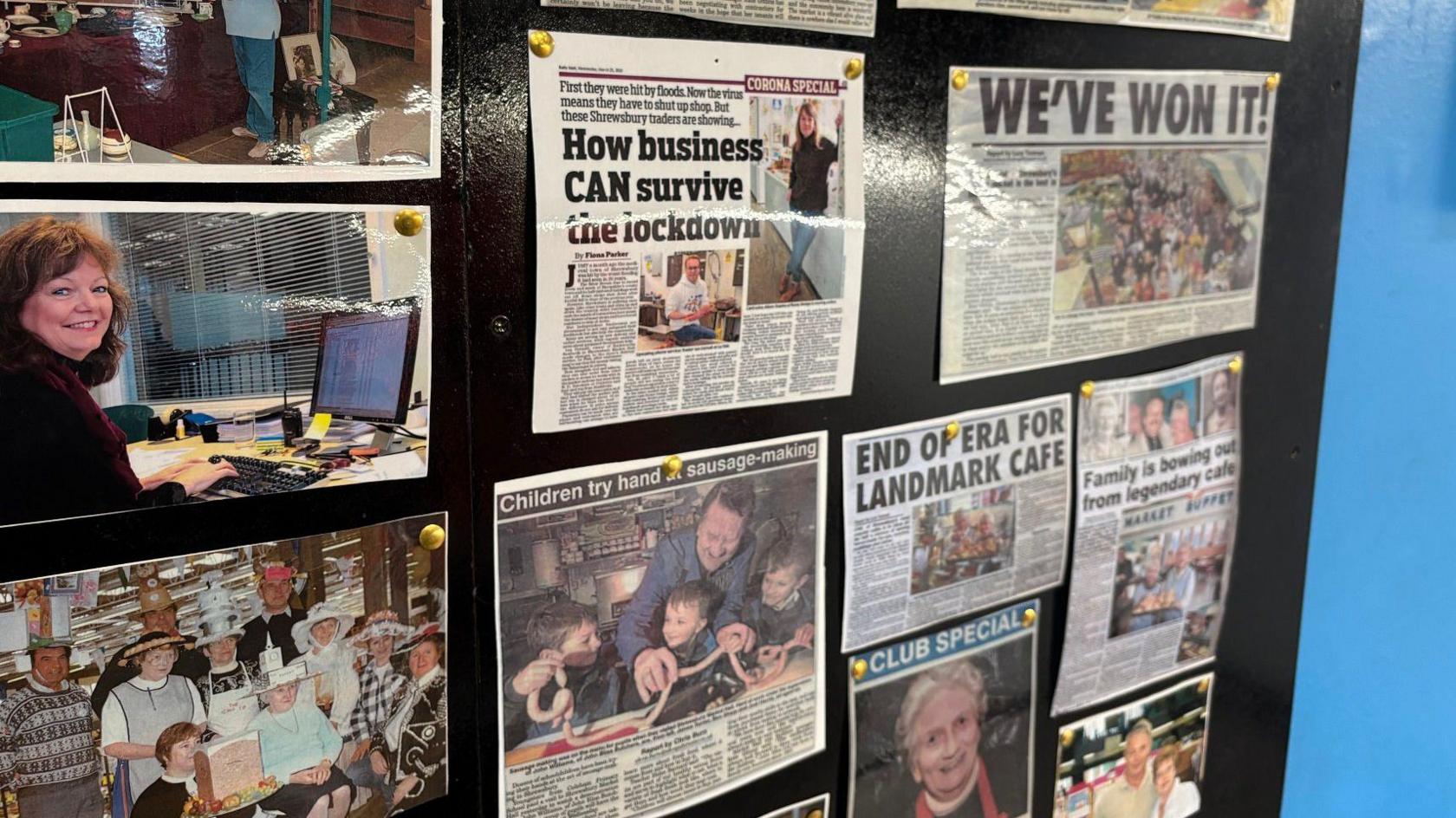 A black board on a wall with photographs and newspaper cutouts on stories from the market over the years. One reads "How business can survive the lockdown", another reads "end of era for landmark cafe"