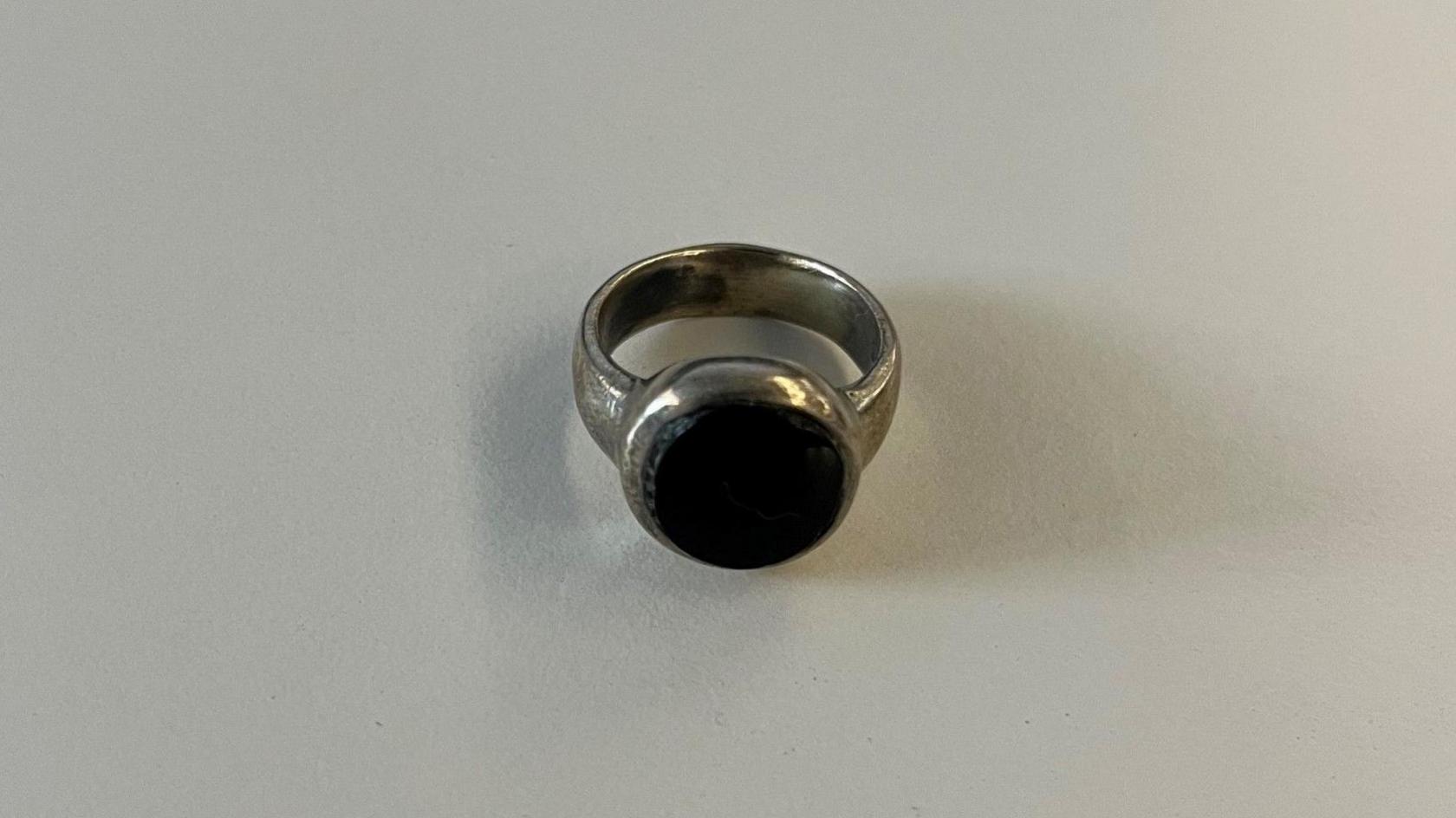 A close up image of a tarnished looking silver ring with a big, black, flat stone in the centre.
