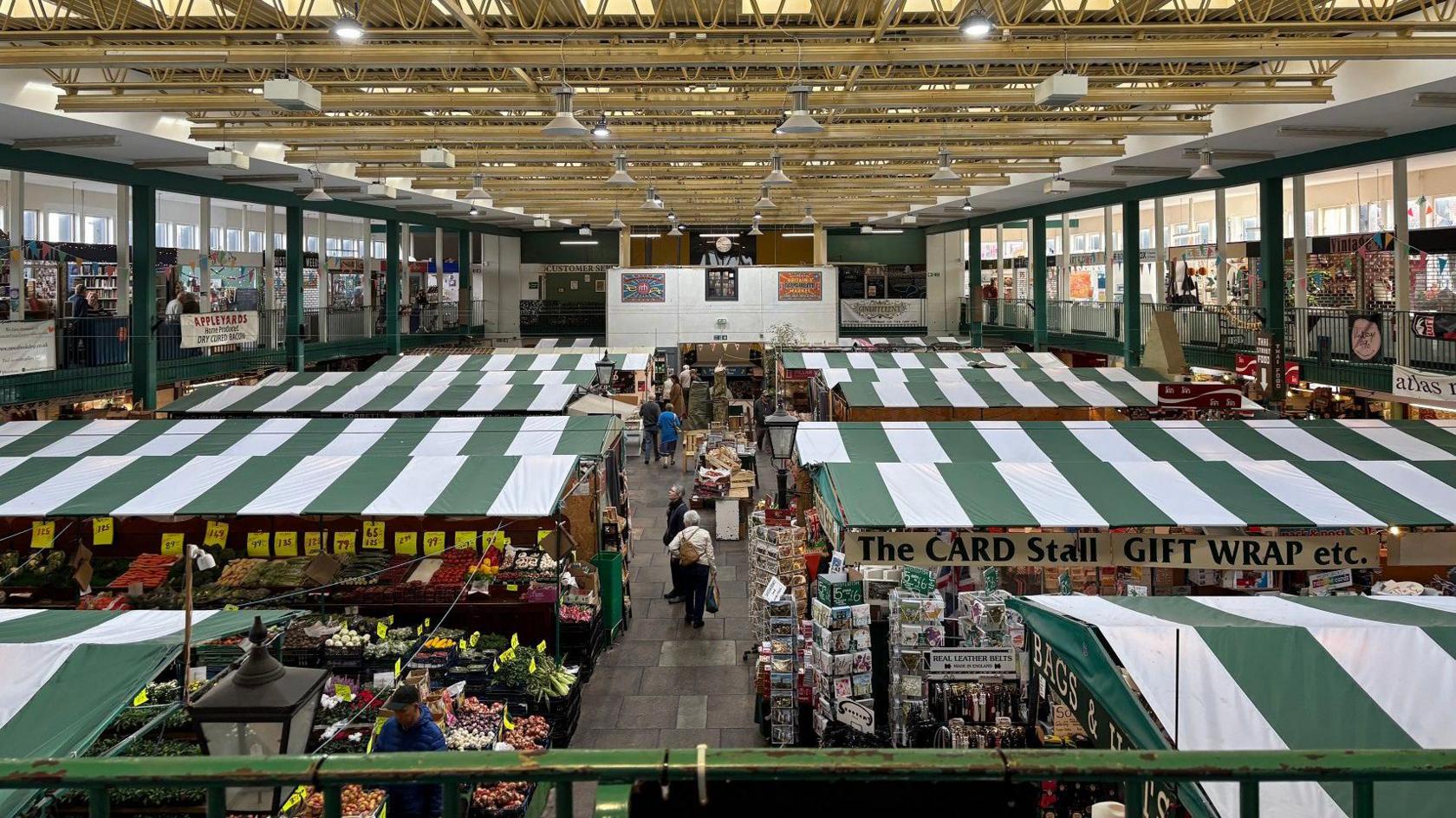 A view from above of the market hall. There are several stall with fabric foors that are green and white striped. One sign reads "the card stall"