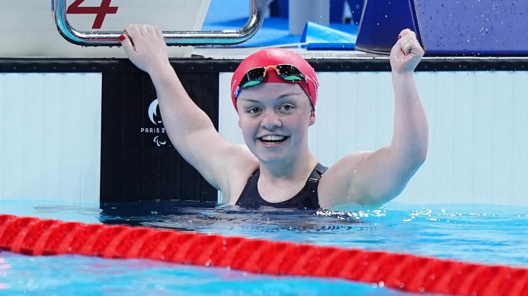 Maisie Summers-Newton raises her arms in the in the swimming pool wearing a red cap