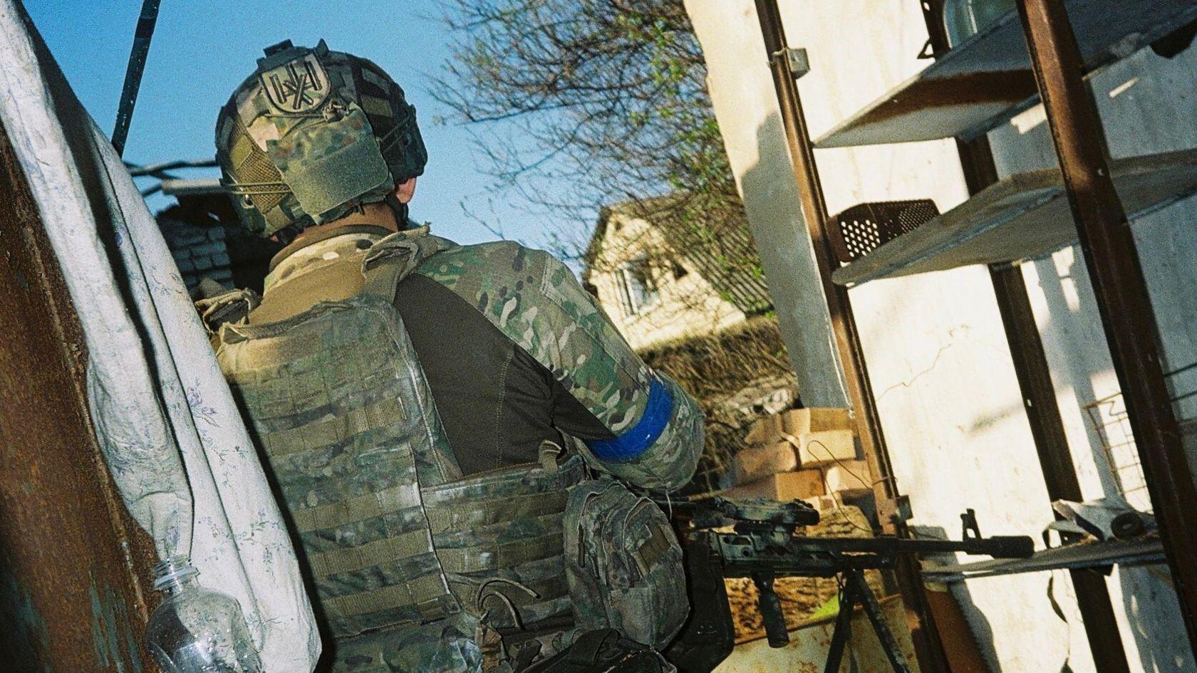 A unformed Ukrainian soldier stands outside, holding a gun