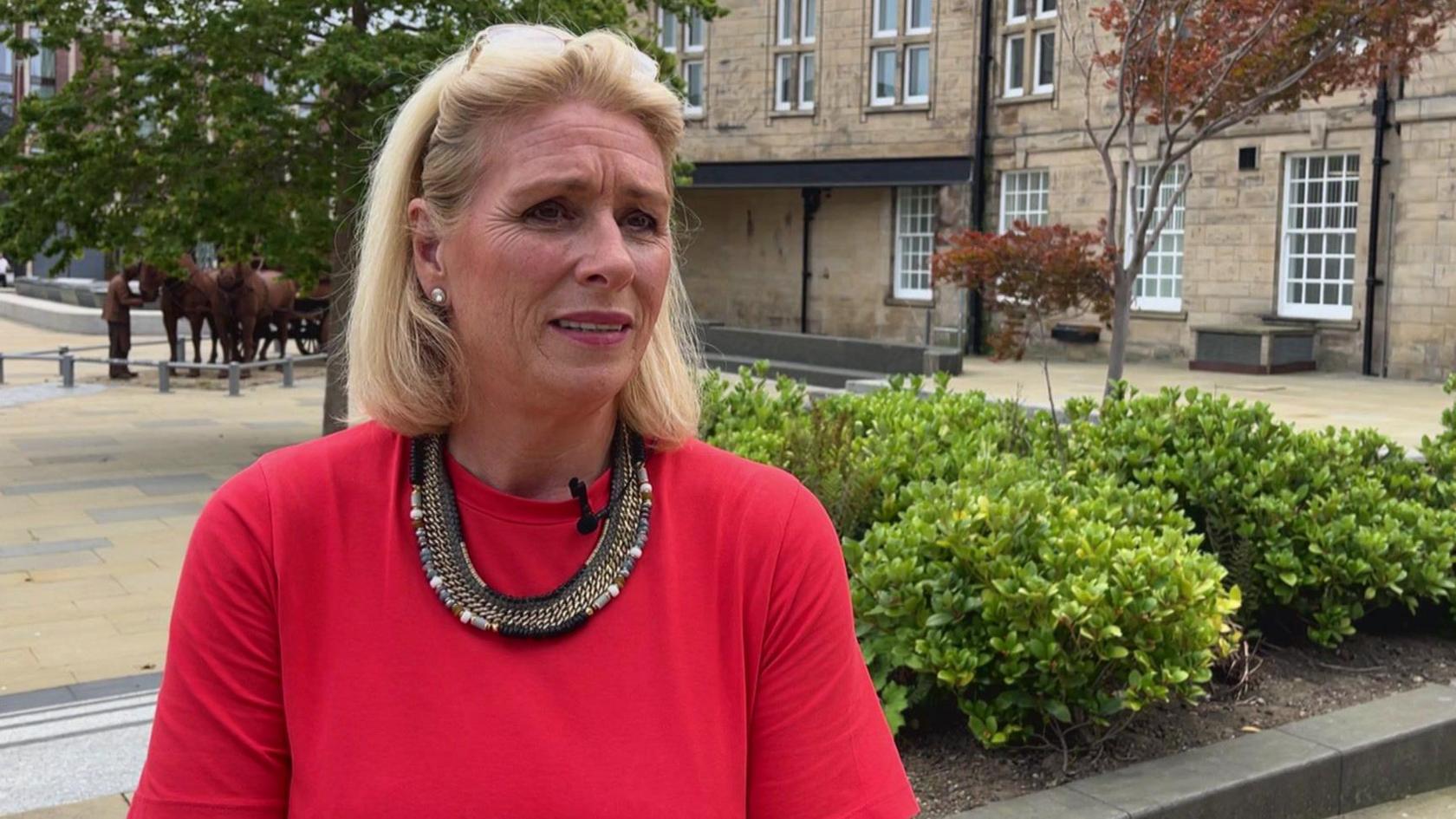 Chief Executive of Sunderland Business Improvement District Sharon Appleby, dressed in a pink dress with a gold and black necklace, stands in front of bushes in Keel Square in Sunderland city centre.