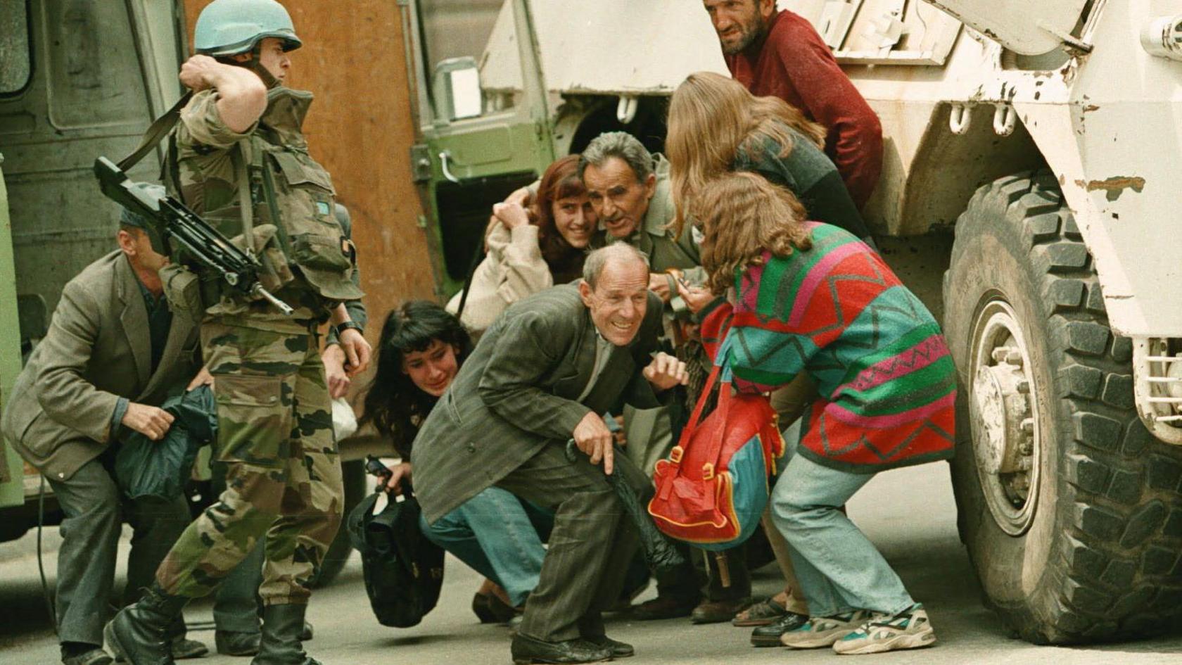 A French U.N. soldier stands alongside a group of Sarajevans seeking shelter behind a French U.N. armoured personnel carrier from sniper-fire after being rescued from their van by French U.N. peacekeepers at a dangerous Sarajevo intersection Thursday June 8, 1995. 