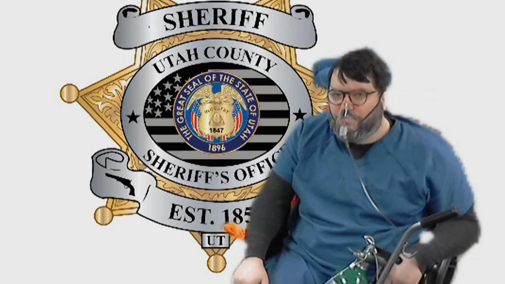 A video link image of Nicholas Rossi in blue prisoner clothes, sitting in a wheelchair in front of an image of the Utah County Sheriff's Office bade. He is wearing an oxygen mask and holding an oxygen bottle in his left hand