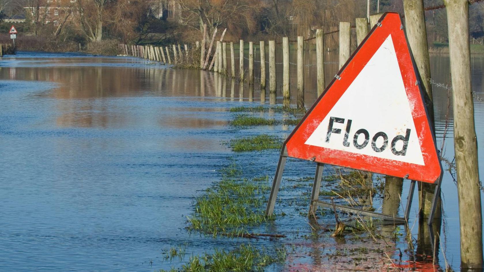 A stock image of a flooded field with a triangular "flood" warning sign.