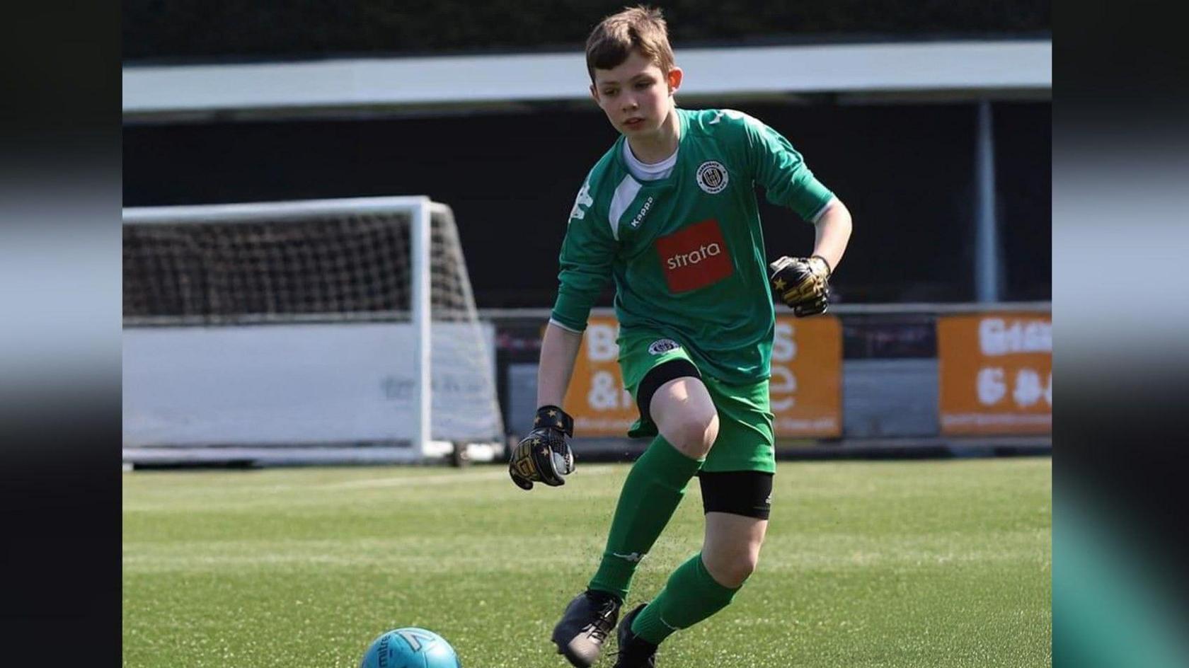 Liam Pinchen as a boy on a football pitch with a ball at his feet and goal behind.