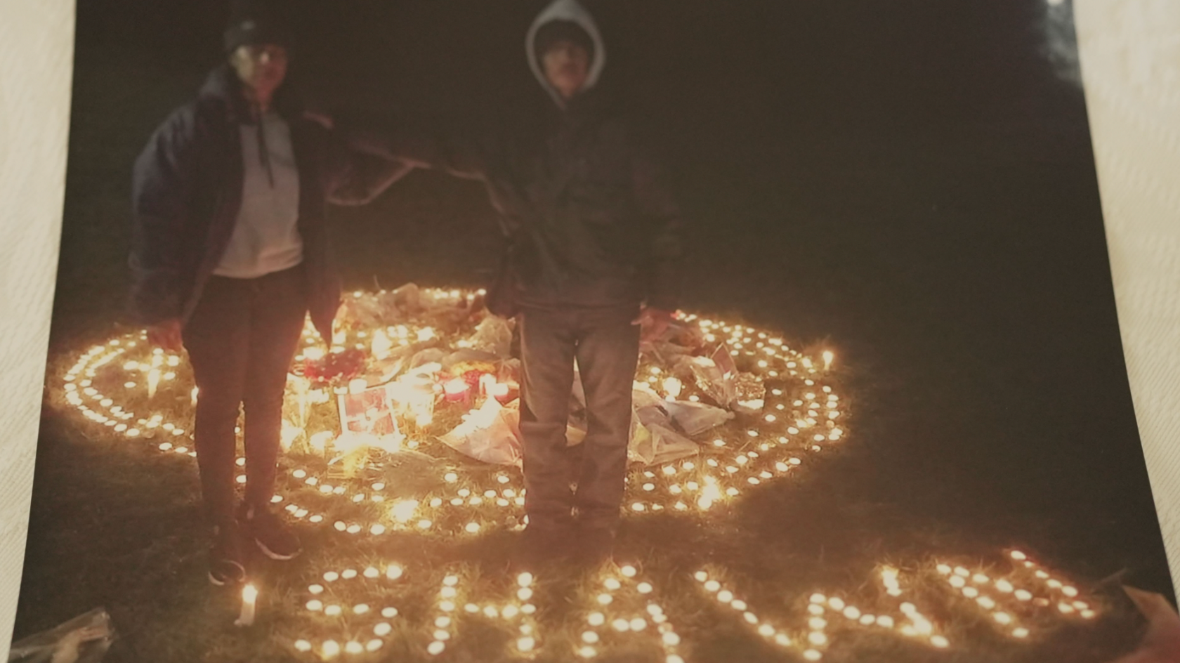 Maneshwary and Suresh standing next to candles spelling Shawn's name