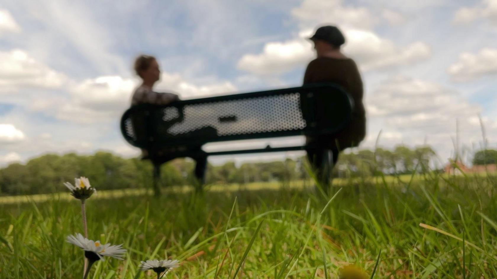 Blurred silhouette of Amanda sitting on a park bench talking to correspondent Nikki Mitchell