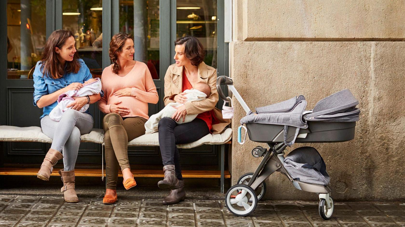 Three women sitting together and chatting with their babies and prams