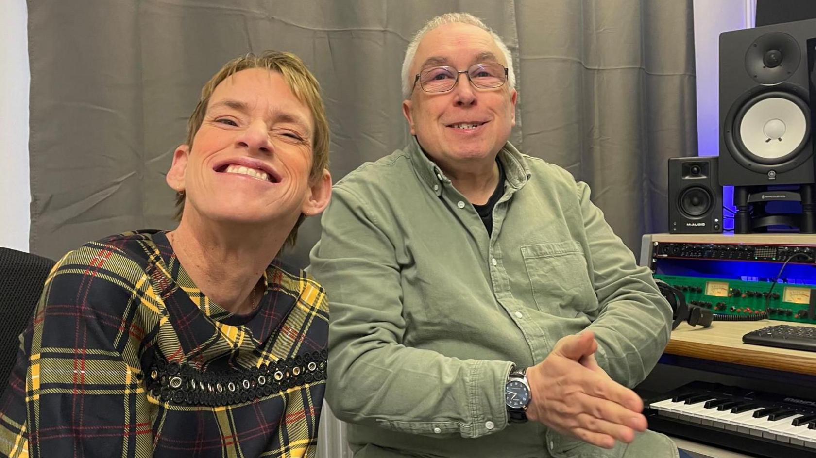 A woman in a yellow dress sits smiling next to a man in a green shirt who sits next to a keyboard