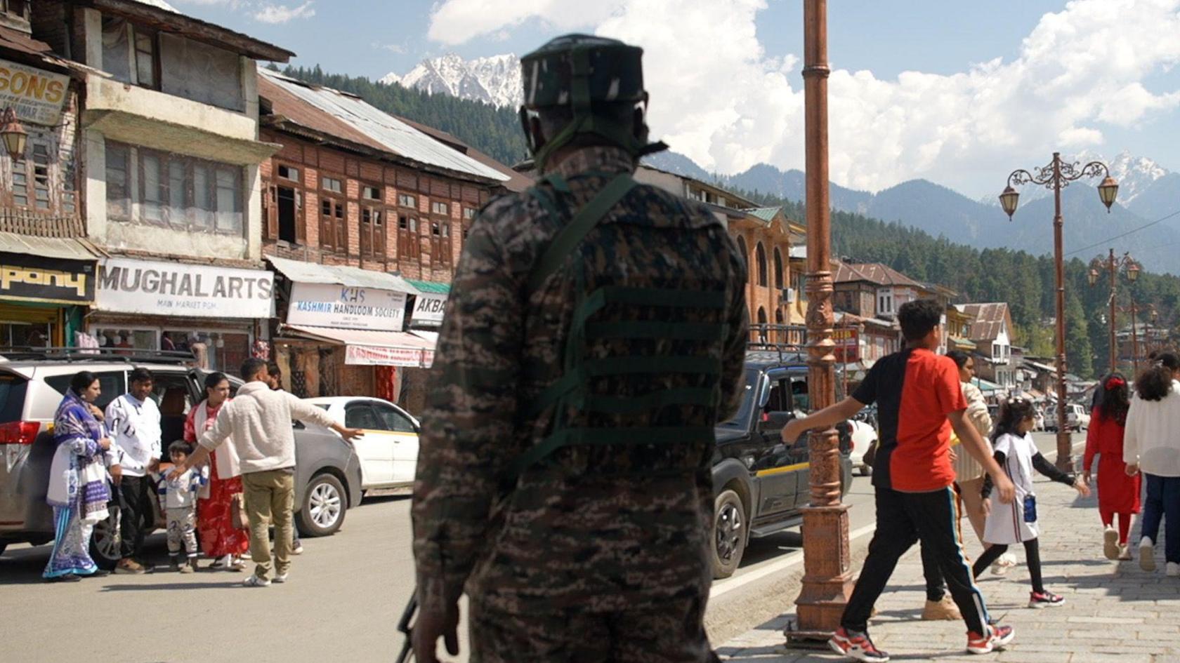 The image shows the main high street in Pahalgam with a few tourists as well as a security personnel in uniform, carrying a gun.