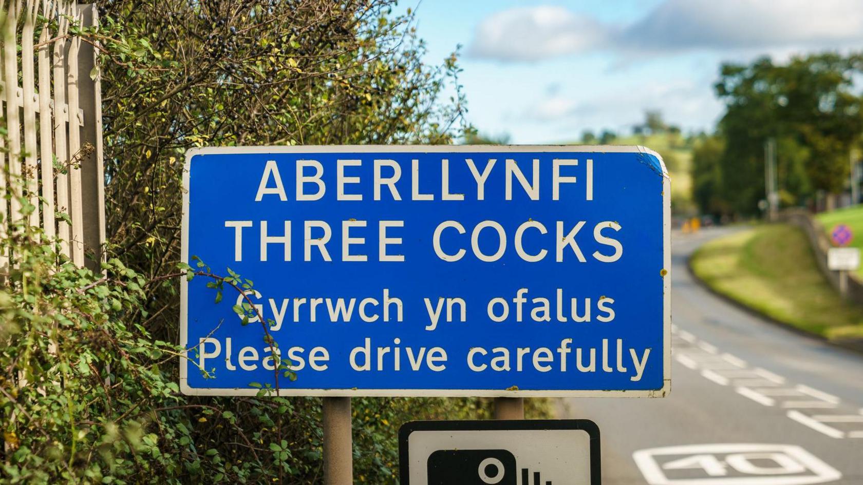 A road sign as you enter Three Cocks village warning people to drive carefully in English and Welsh.