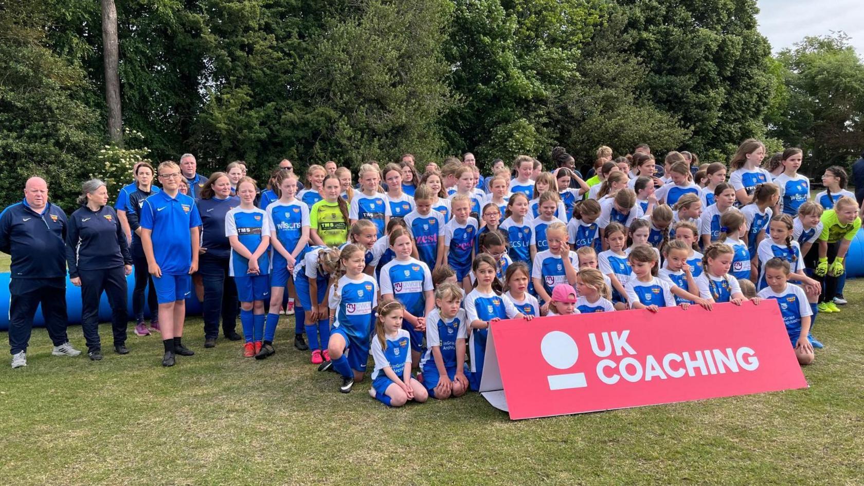 Dozens of young football players in blue and white kits gathered in a field for a photograph