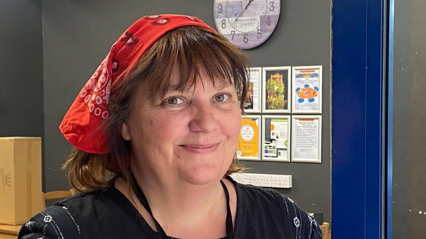 Karen Davis was stood looking towards the camera with a light smile. She had shoulder length brown hair and was wearing a red bandana and a black top.