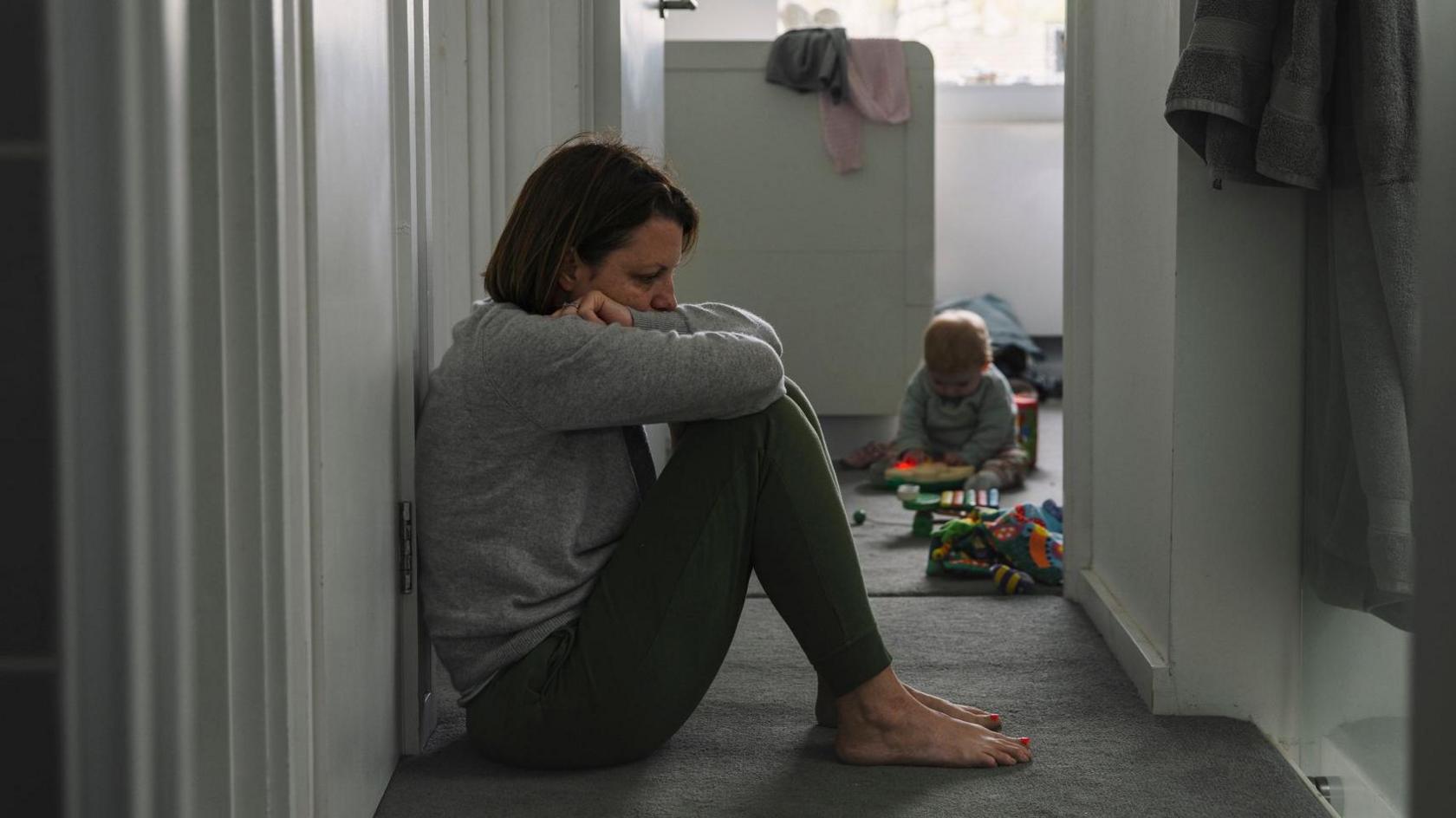 Generic picture of a mother sitting on the floor with her baby in the background