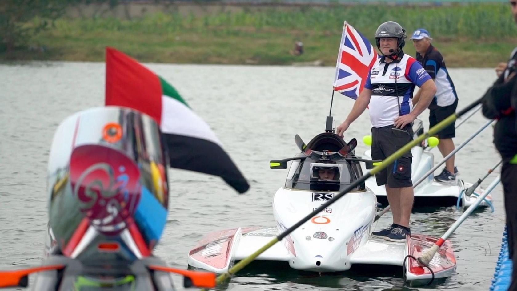 Ben Jelf in the driver's seat of the boat, next to his father Colin, who is standing on the boat's left wing