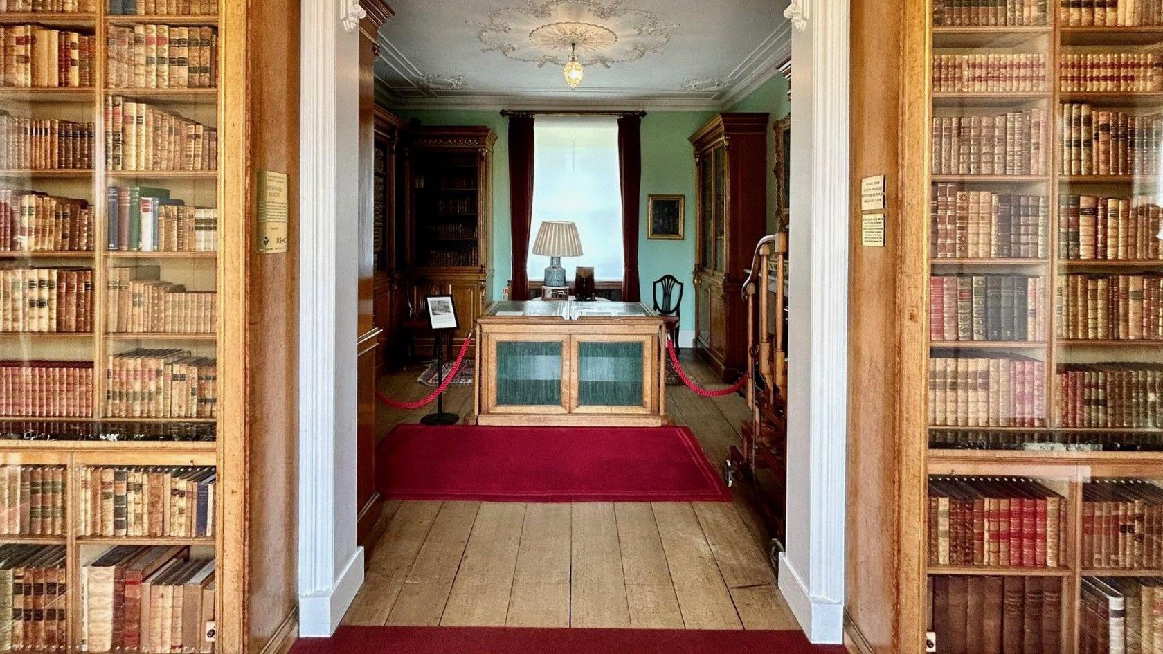 An open doorway in a stately home surrounded by books looking into a smalled room also with bookshelves