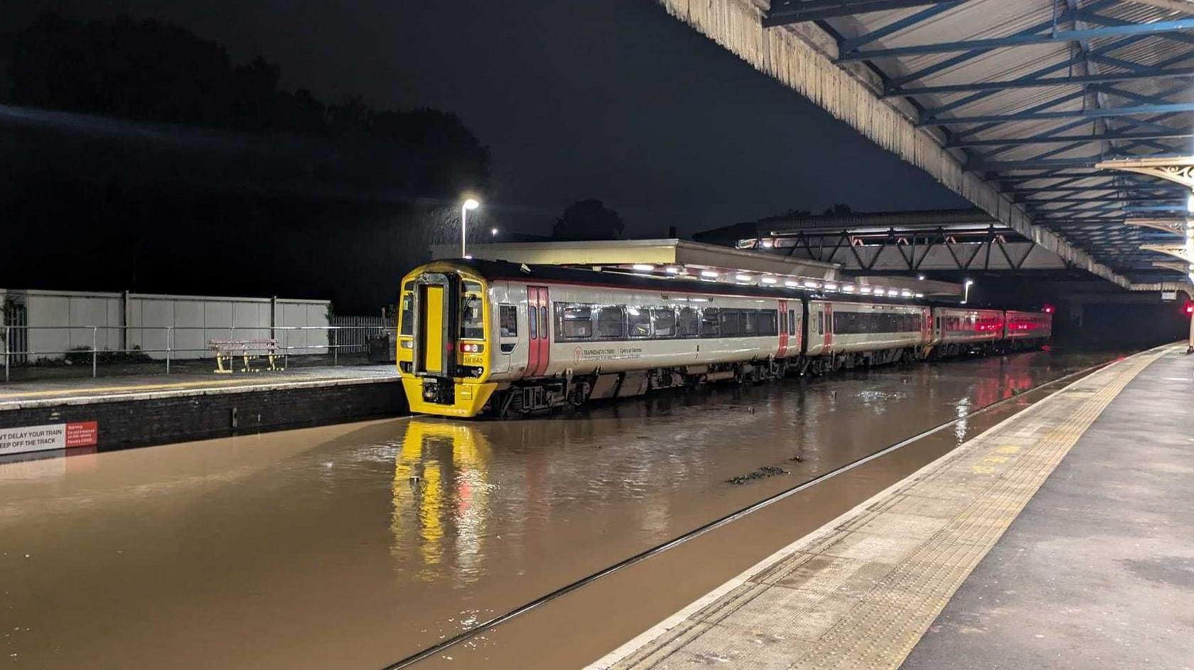 A train at a train station with the tracks completely submerged by brown flood water