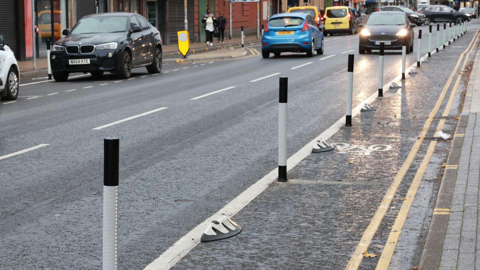 A section of the Linthorpe Road cycle lane which is marked by a solid white line and black-and-white poles. Cars are driven on the road to the left of the cycle lane.
