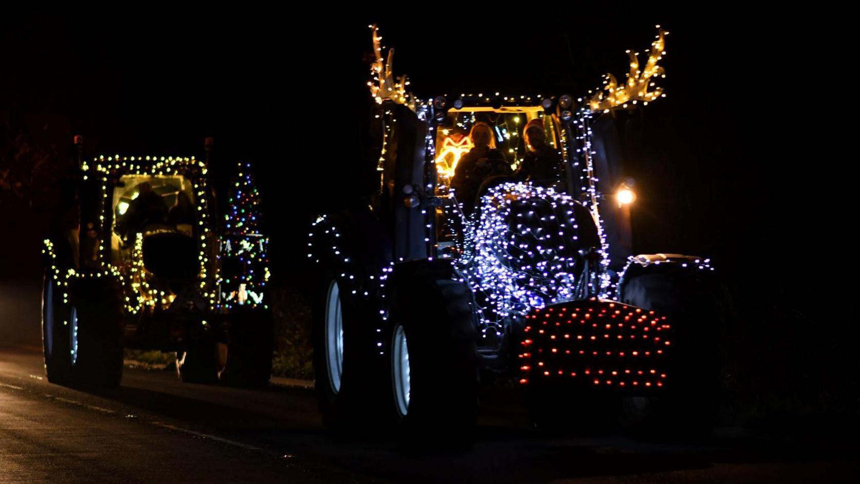 Two tractors covered in an array of festive fairy lights in the middle of a road.