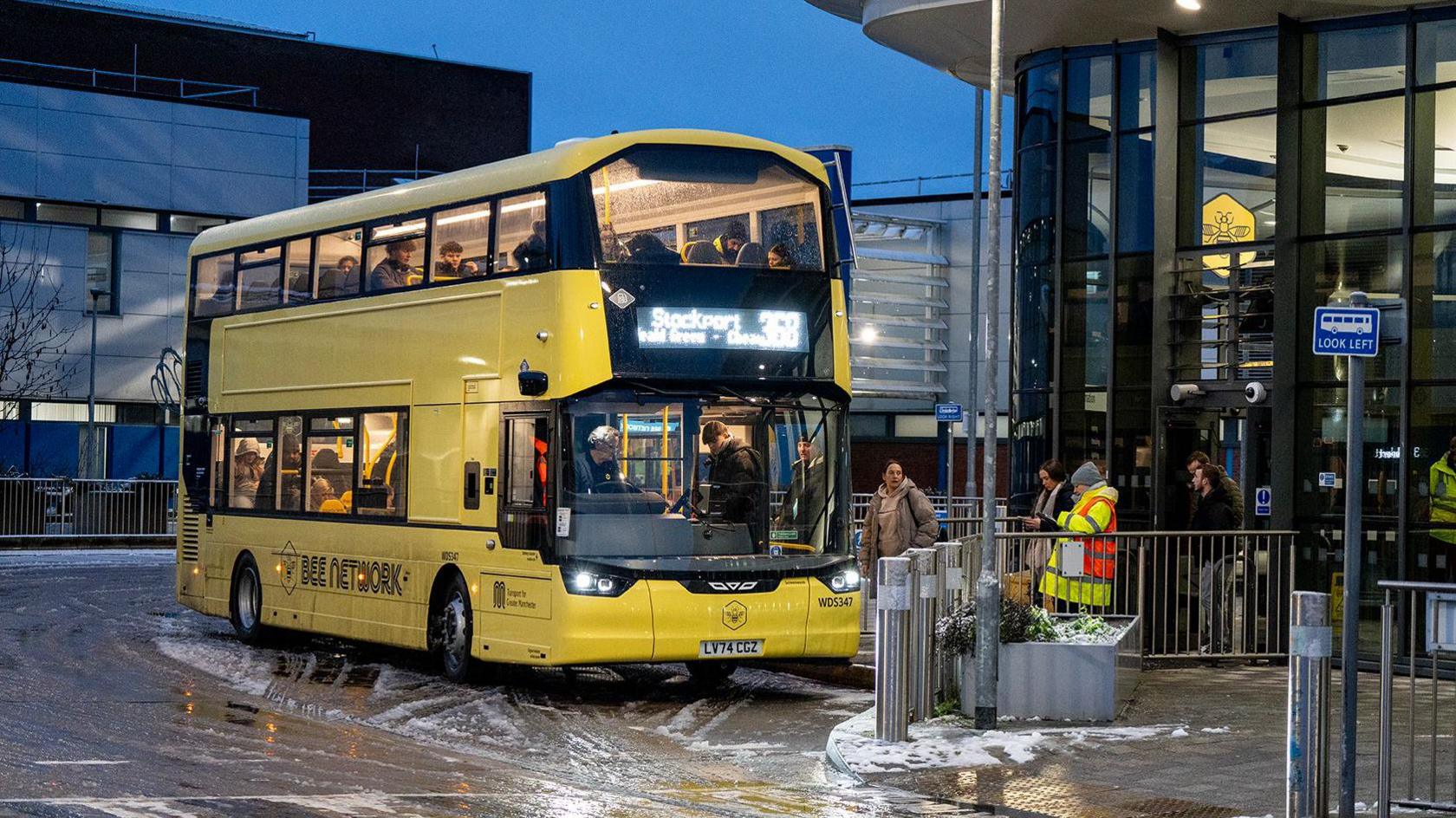 Passengers get on a Bee Network bus at Wythenshawe Interchange. The bus is parked with slush seen on the road. 