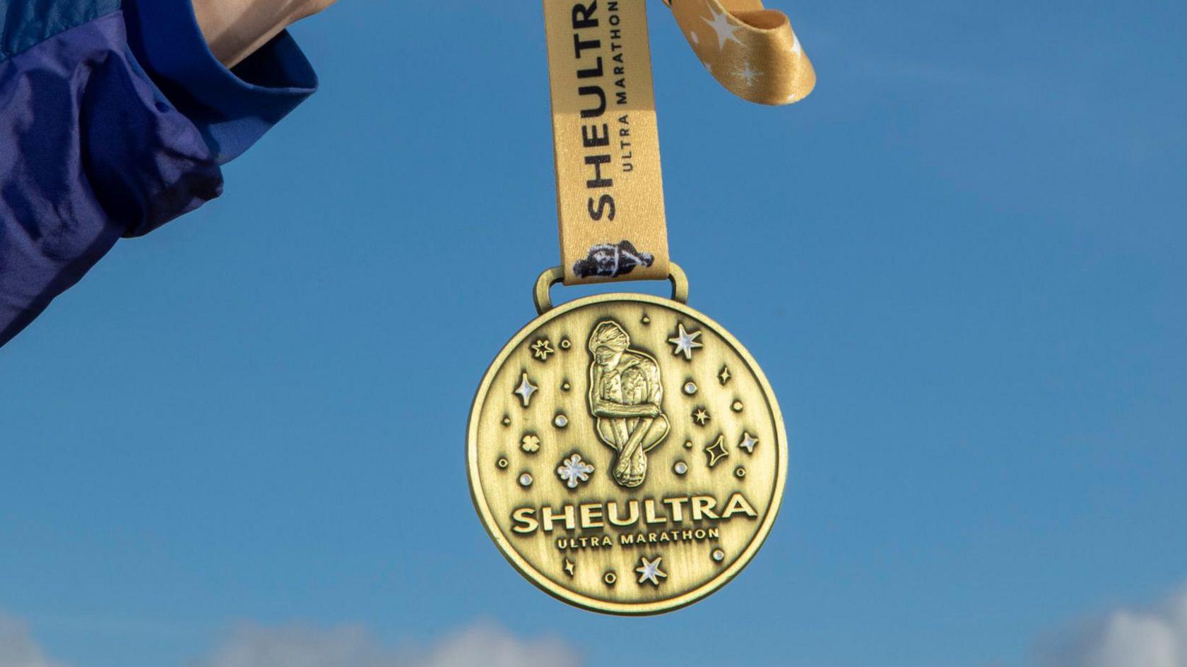 Medal aur gyda geiriau 'Sheultra - ultra marathon' wedi'u hysgrifennu arno